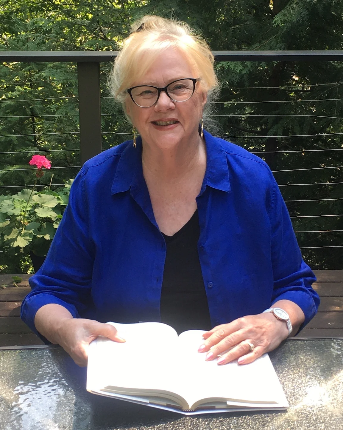 A woman, Kathleen Kaiser, in a blue shirt reading an open book outdoors.